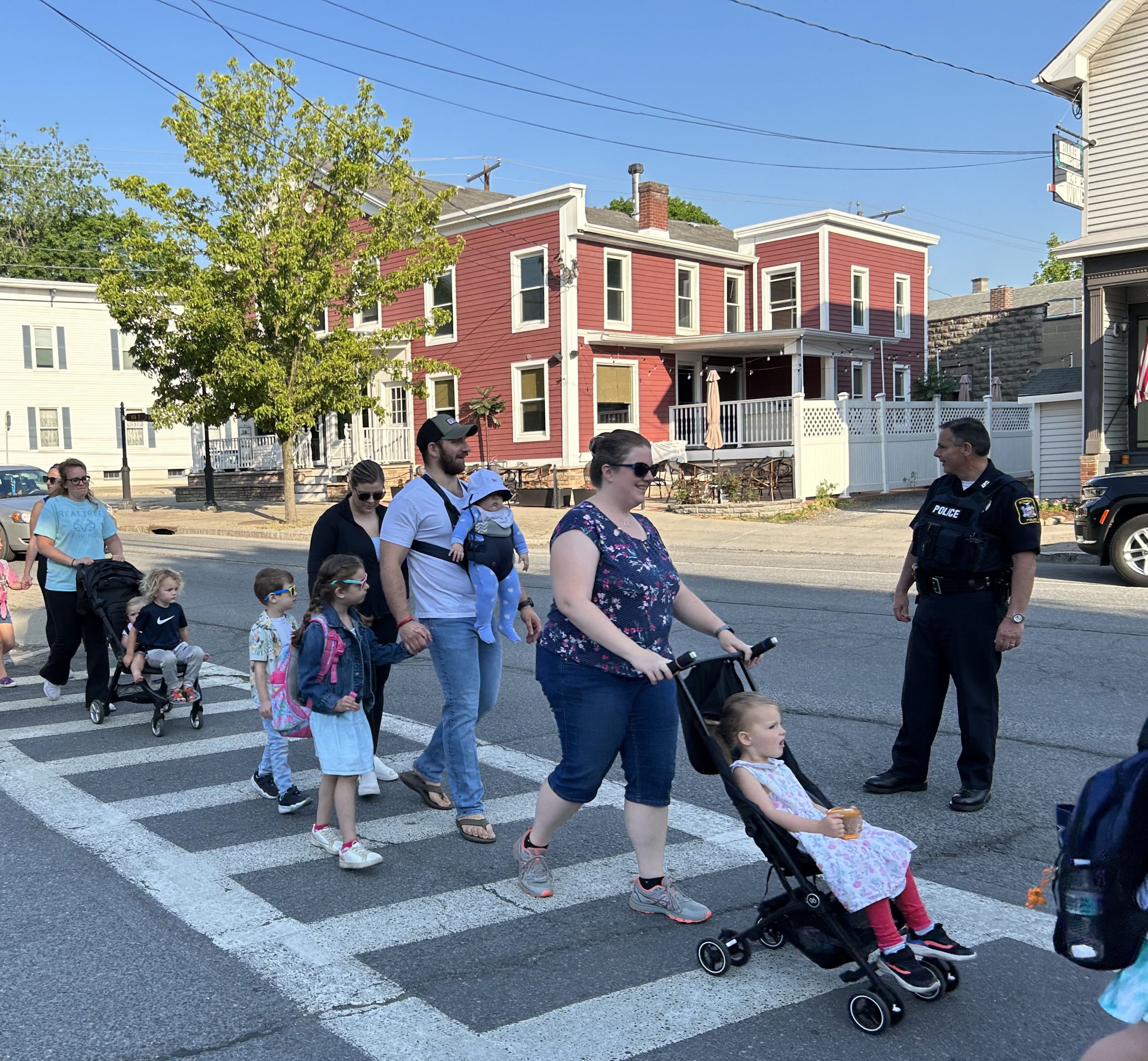 Students and families cross a street while walking to school. One parent pushed a child in a stroller.