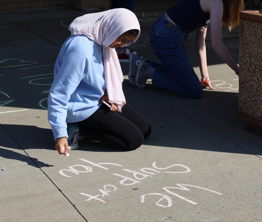 Student writes the words "we support you" in chalk at the GHS Anti-Hate Rally