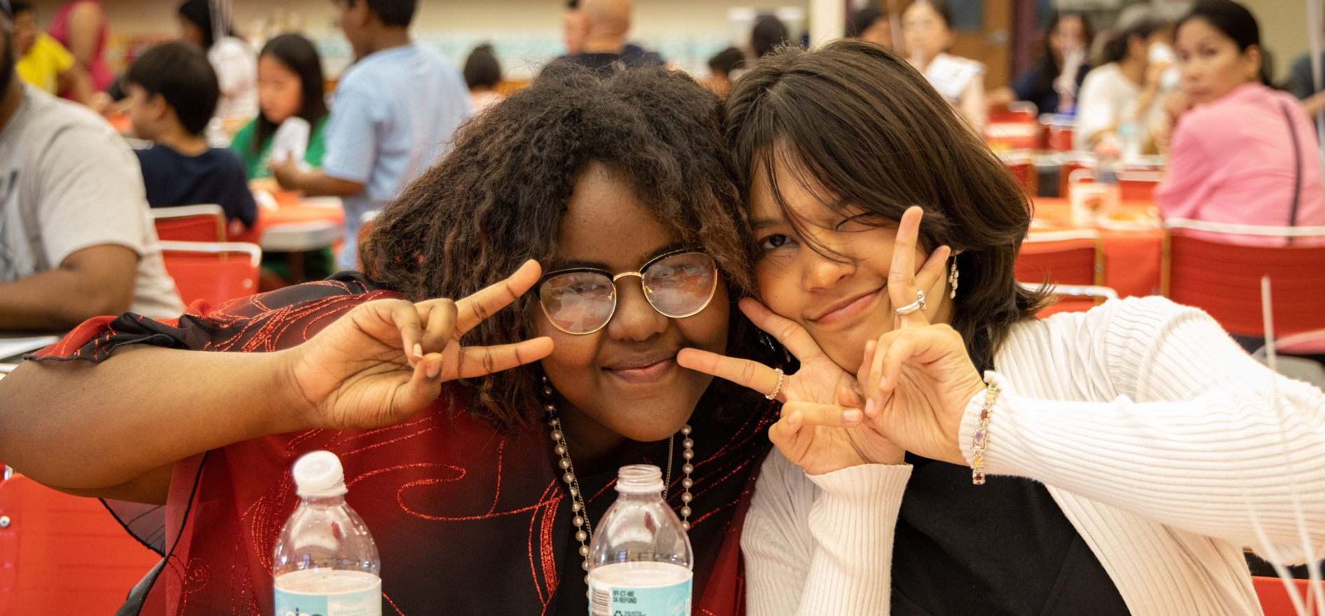Two students make peace signs and smile while sitting at the dinner table at ENL Extravaganza