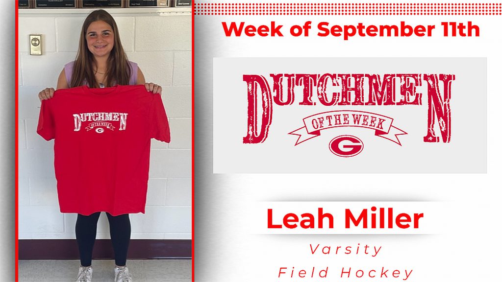 Student stands in front of a white wall holding a white t-shirt with red lettering that reads Dutchmen of the Week
