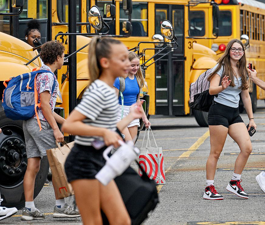 One student is waving as others exit from the school bus.