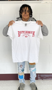 Student stands in front of a white wall holding a white t-shirt with red lettering that reads Dutchmen of the Week