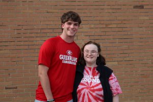 Two students stand in front of a brick wall. They are smiling at the camera. Each is wearing a t-shirt that represents unified athletics.