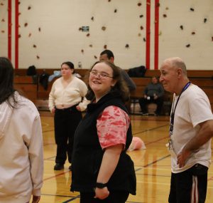 Student is standing in a gym, she is turning to smile at the camera. Others are standing around her