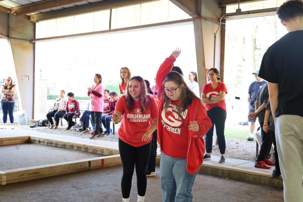 Two students playing bocce, one has her hand raised in the air, one is pointing at the shot