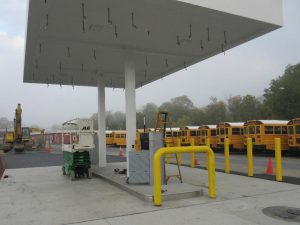 Yellow school buses are in the background. Fuel island is in the foreground. It is under construction.