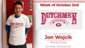 Student stands in front of a white wall, holding a red t-shirt with white text that reads Dutchmen of the Week