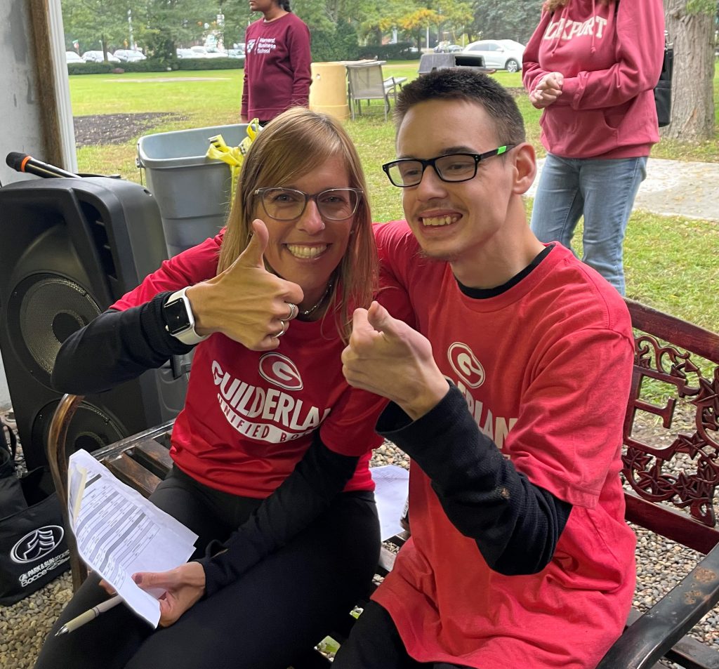 A teacher and a student wearing red t-shirts smile with thumbs up.