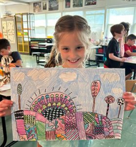 Student is smiling at the camera, holding a colorful piece of artwork