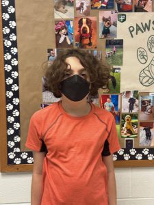 Student is wearing a mask, standing in front of a bulletin board