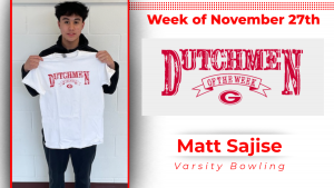 Student stands in front of a white wall and is holding a white t-shirt with red writing that says Dutchmen of the Week