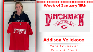Student stands in front of a white cinder block wall holding a red t-shirt with white text that reads Dutchmen of the Week