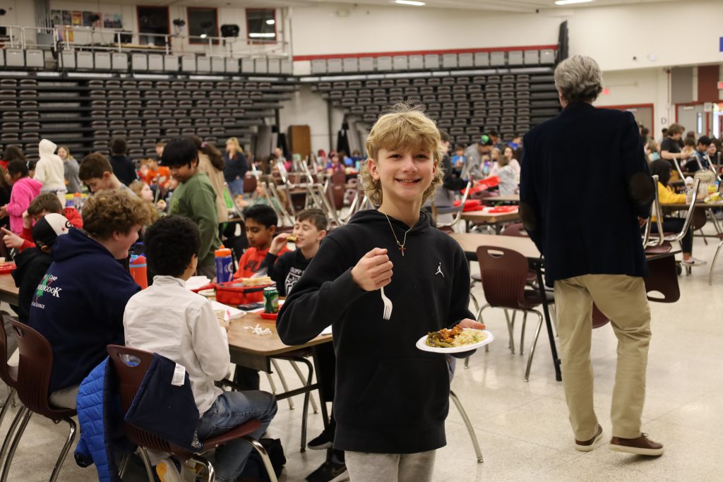 Student smiling with a "thumbs up" while holding a plate of food.