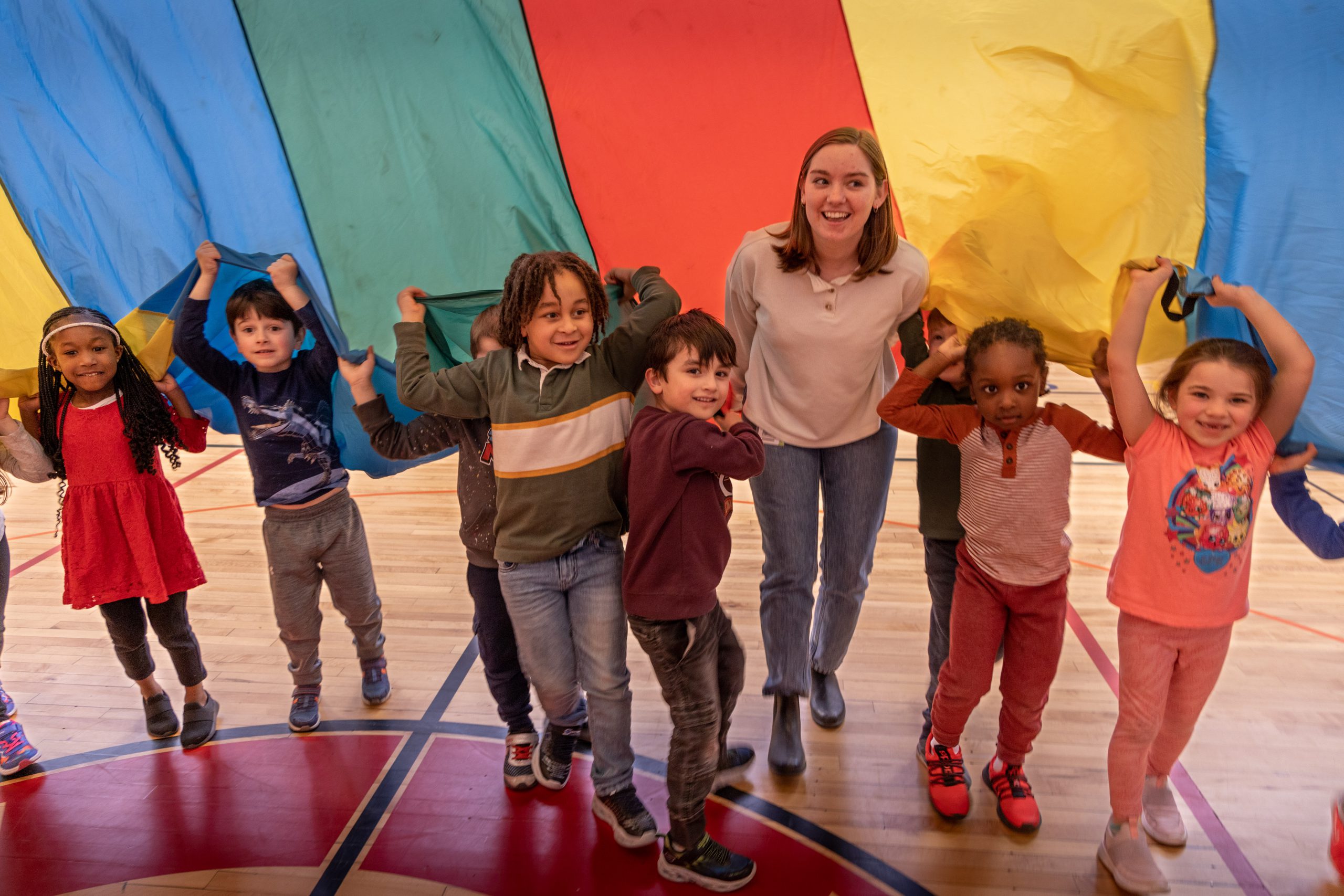 A teacher and a group of elementary students are under a rainbow striped tarp