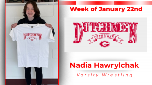 A student stands in front of a white wall holding a white t-shirt with red lettering that reads Dutchmen of the Week