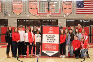 A group of students and teachers stand in a gym with a banner that reads Special Olympics, National Unified Champion School Guilderland High School 2022-2026