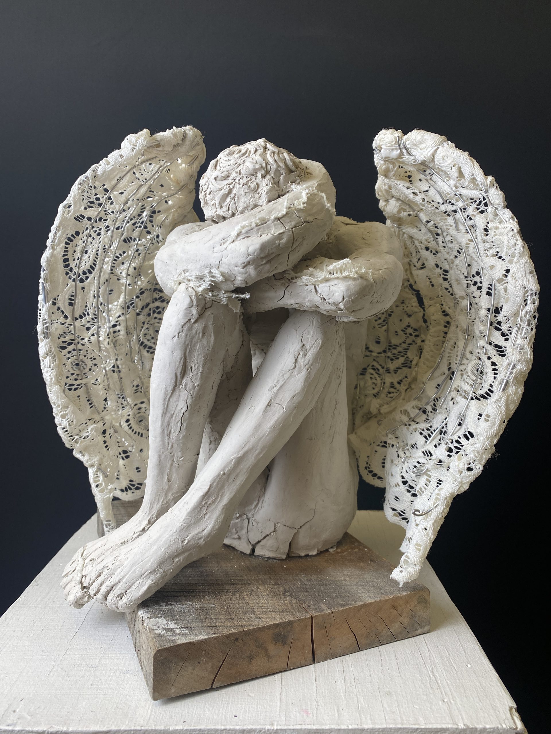 Student artwork: a sculpture of an angel sitting down with hands crossed on knees, head down