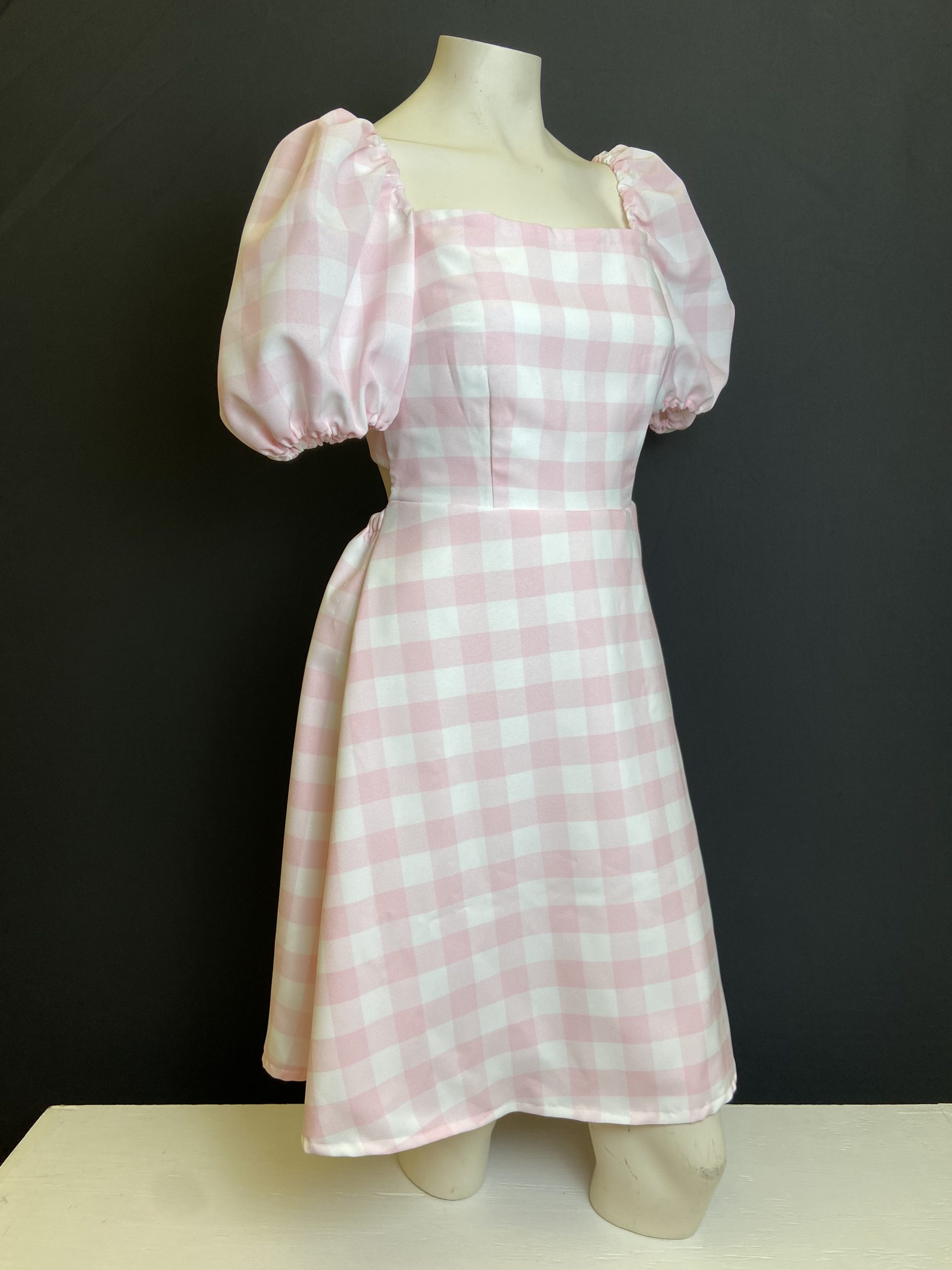 A pink and white gingham dress on a mannequin without a head and arms.