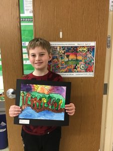 A student stands in front of a classroom door, holding a piece of artwork he created