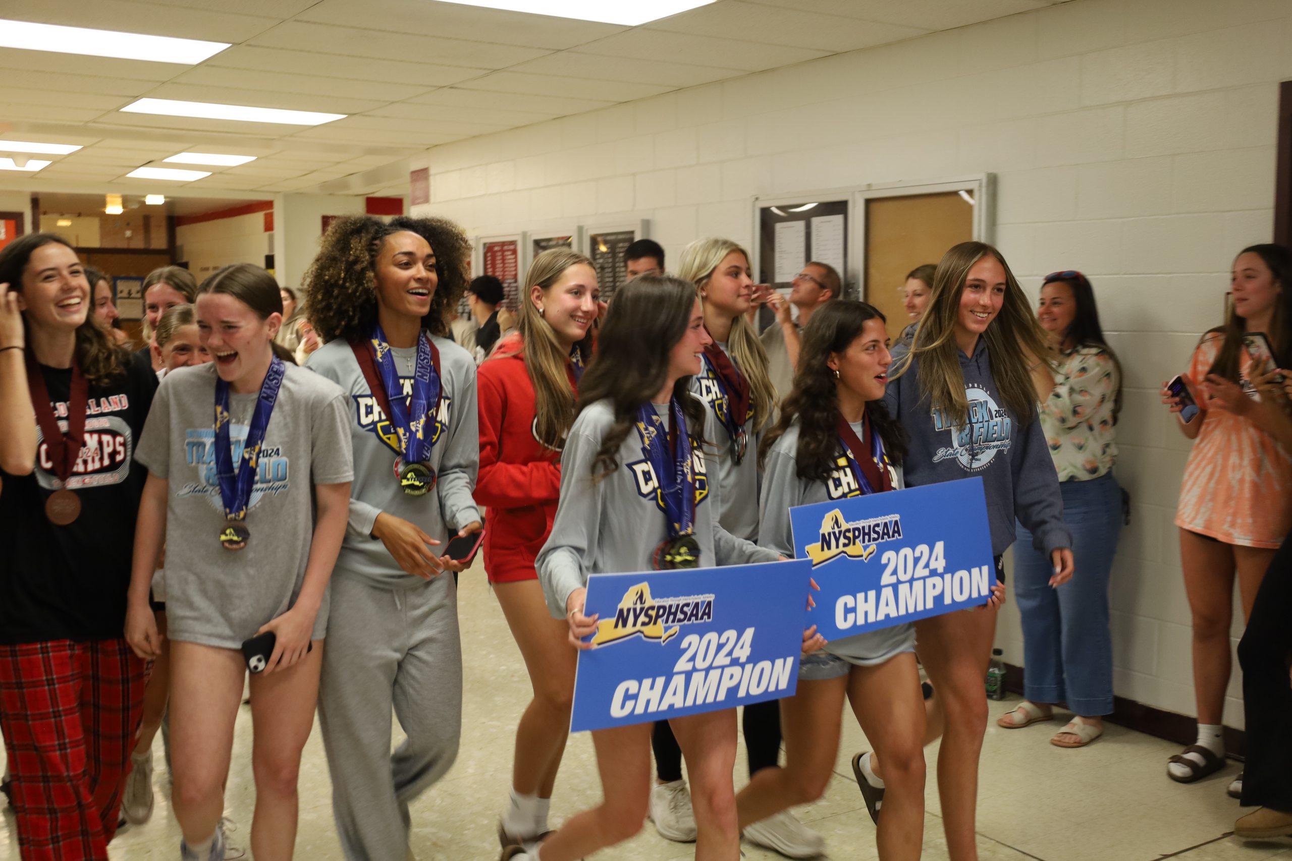 Track and field athletes walk the halls of GHS holding signs and balloons. Students are lining the halls, applauding