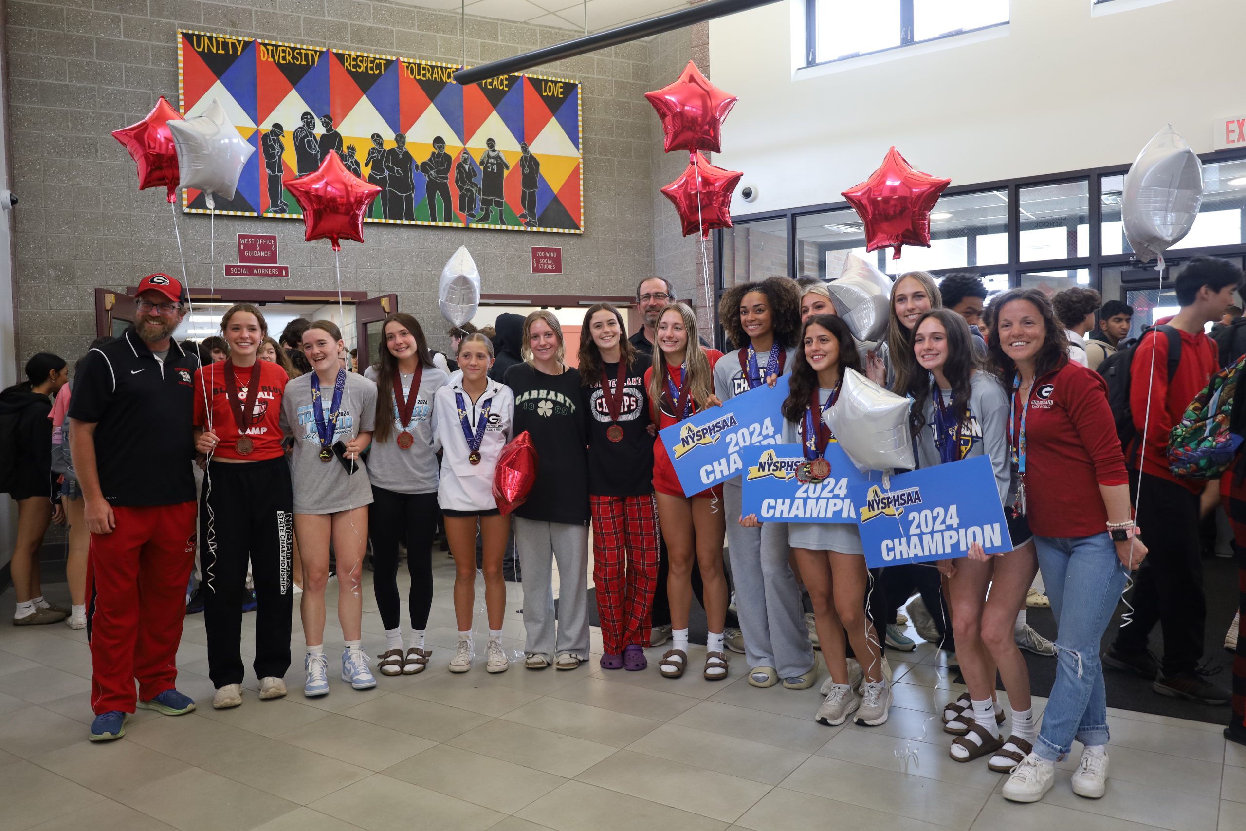 Students stand in a line with coaches, holding balloons and signs