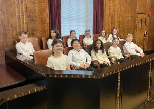 Elementary students sitting in two rows of a jury box.