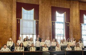 The LES Chorus posing for a group photo with U.S. District Judge Daniel J. Stewart in a room of the U.S. Courthouse with light shining through the windows behind them.