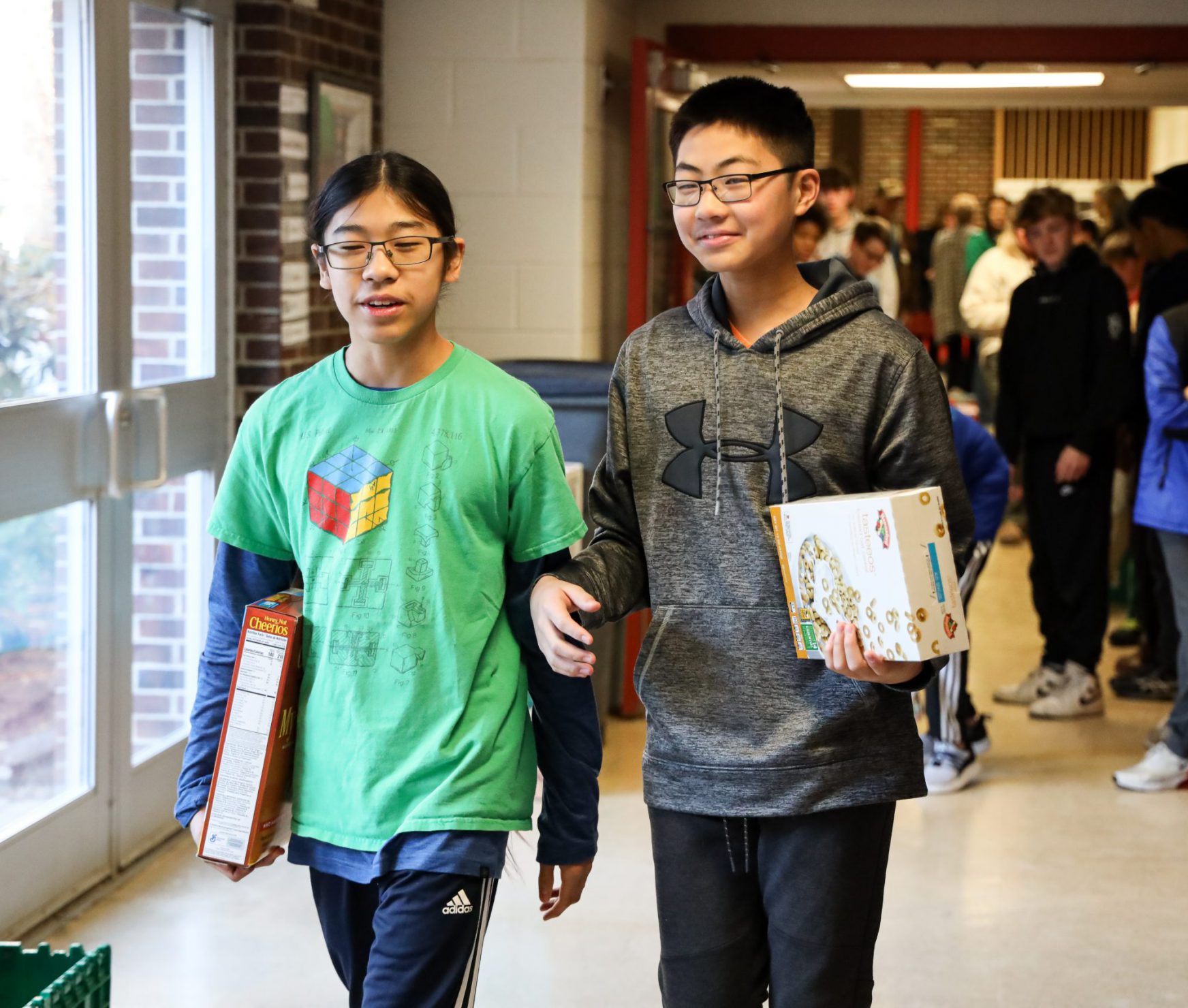 Two FMS students preparing for the cereal box dominoes event. They are holding cereal boxes and walking through the halls together.