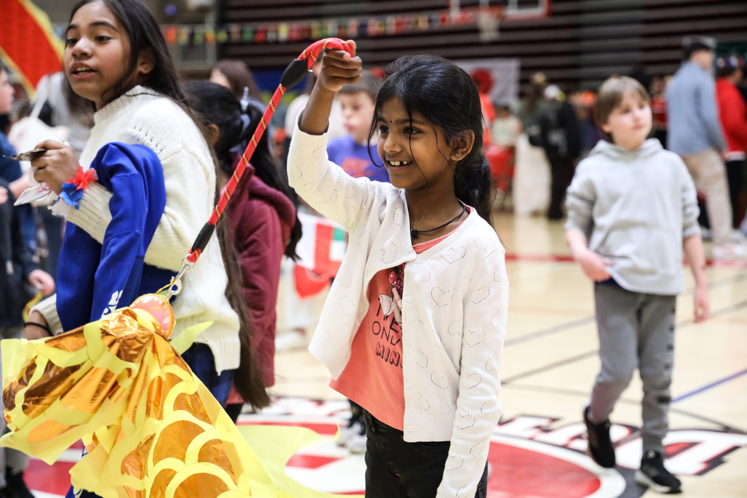 A young student is smiling, standing in a gym, holding something