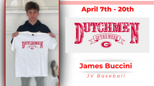A student stands in front of a white wall, holding a white t-shirt with red lettering that reads "Dutchmen of the Week."