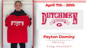 A student stands in front of a white wall, holding a red t-shirt with white lettering that reads "Dutchmen of the Week."