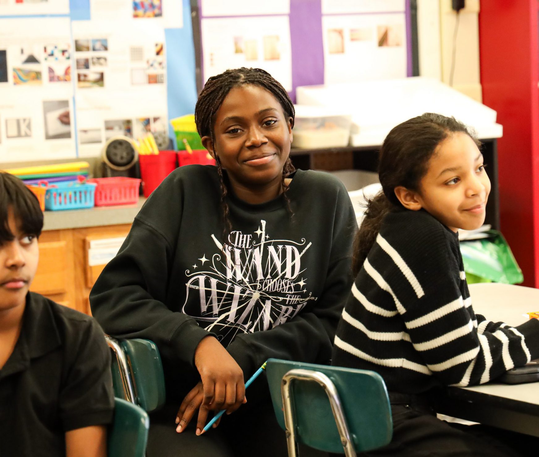 Student smiling in class. She is sitting at her desk and looking at the camera.