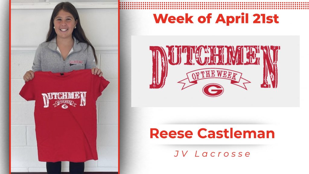 A student stands in front of a white wall, holding a red t-shirt with white lettering that reads "Dutchmen of the Week."
