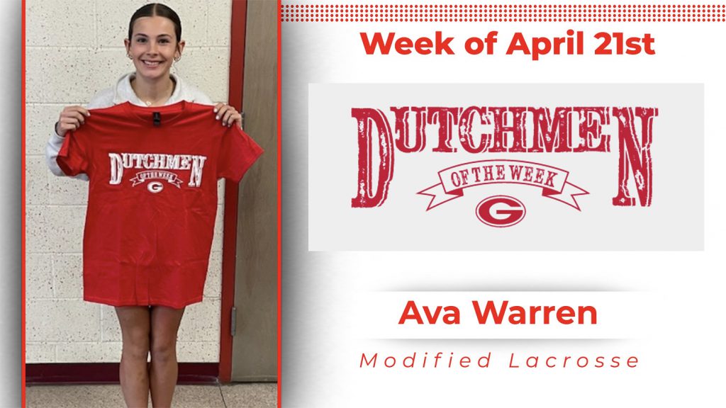 A student stands in front of a white wall, holding a red t-shirt with white lettering that reads "Dutchmen of the Week."