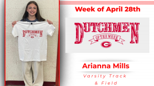 A student stands in front of a white wall, holding a white t-shirt with red lettering that reads "Dutchmen of the Week."