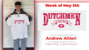 A student stands in front of a white wall, holding a white t-shirt with red lettering that reads "Dutchmen of the Week."