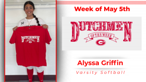 A student stands in front of a white wall, holding a red t-shirt with white lettering that reads "Dutchmen of the Week."
