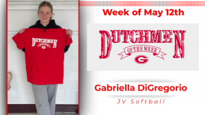 A student stands in front of a white wall, holding a red t-shirt with white lettering that reads "Dutchmen of the Week."