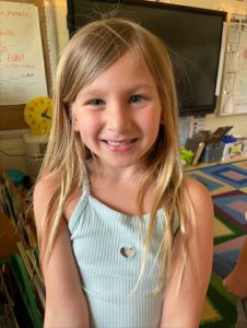 A close up shot of a young student in a classroom, smiling at the camera