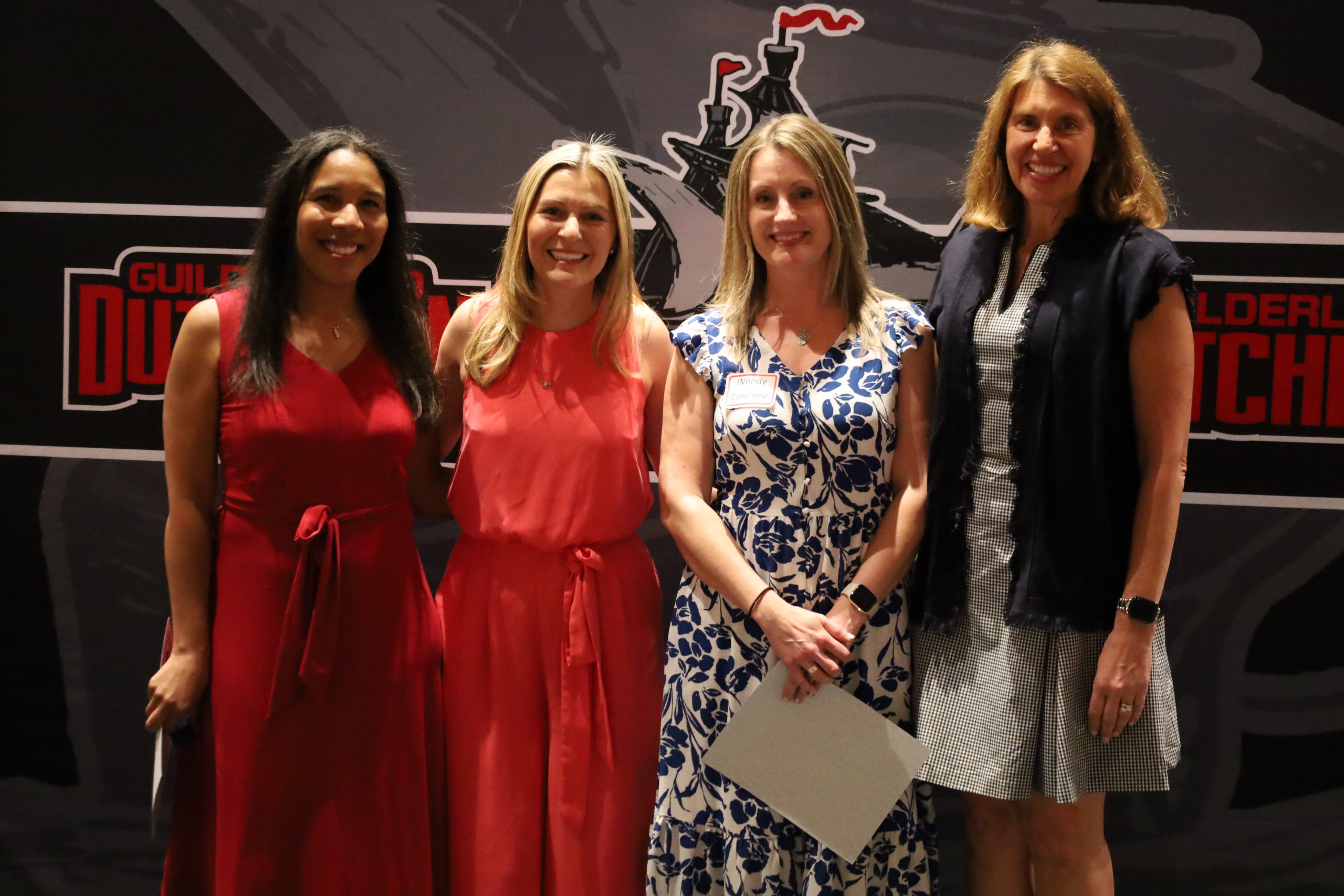 Four people stand in front of a backdrop, they are smiling.