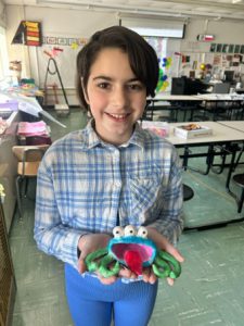A student stands in a classroom holding a three-dimensional piece of art