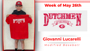 A student athlete stands in front of a white wall holding a red t-shirt with white lettering that reads"Dutchmen of the Week"