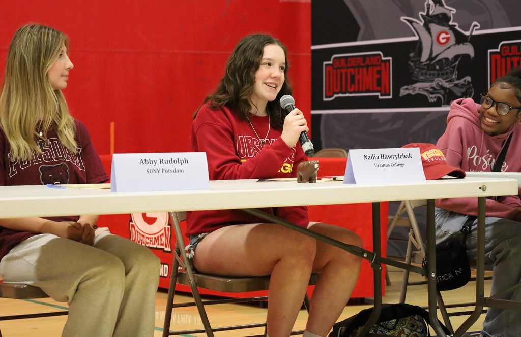GHS student speaking into the microphone. She's sitting at a table with a white name card in front of her.