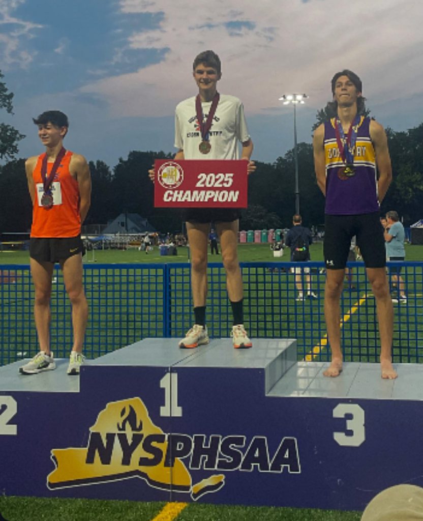 Three athletes standing on the NYSPHSAA podium that has first place in the middle, second place on the left and third place on the right. The GHS male athlete is standing on the first place spot holding a red "2025 Champion" sign in his hands.