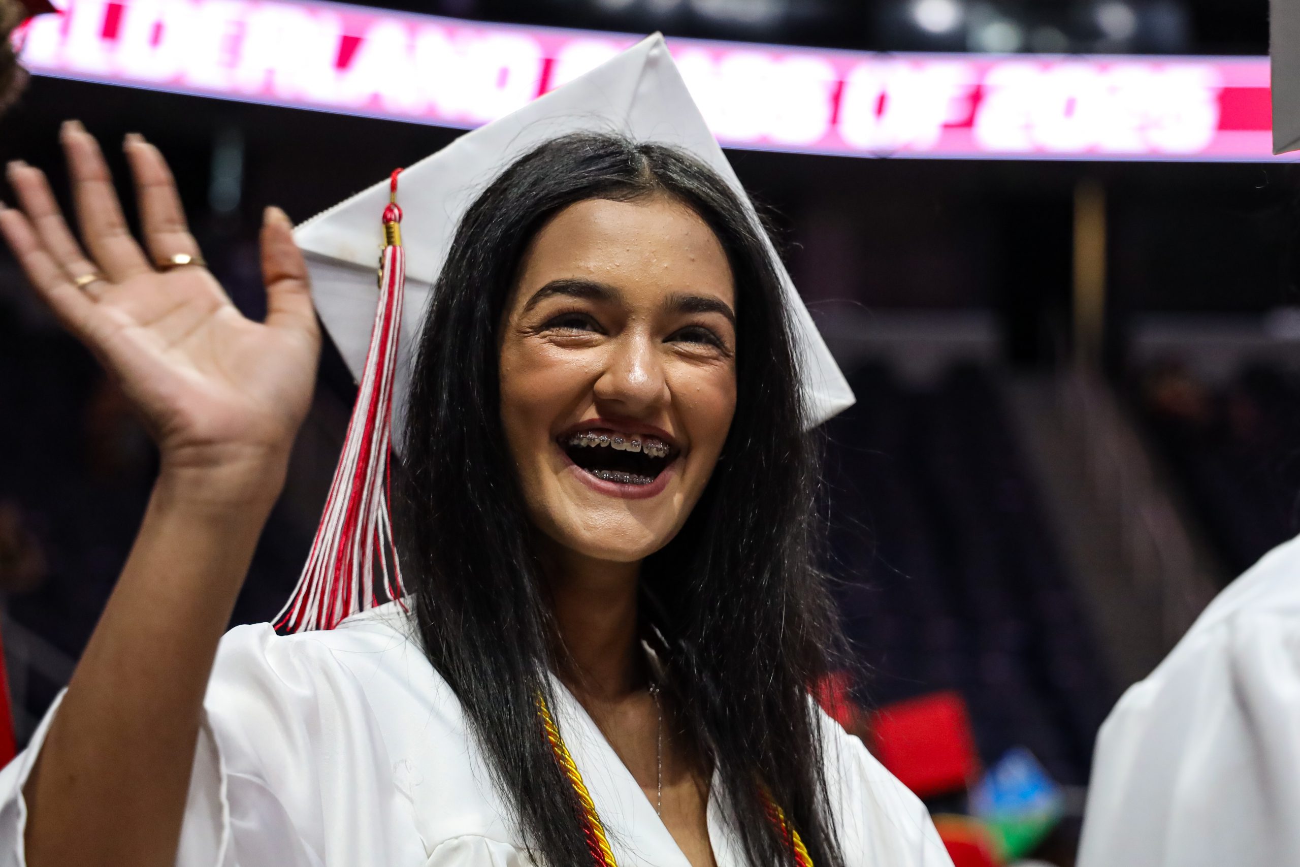 A graduate is smiling and waving
