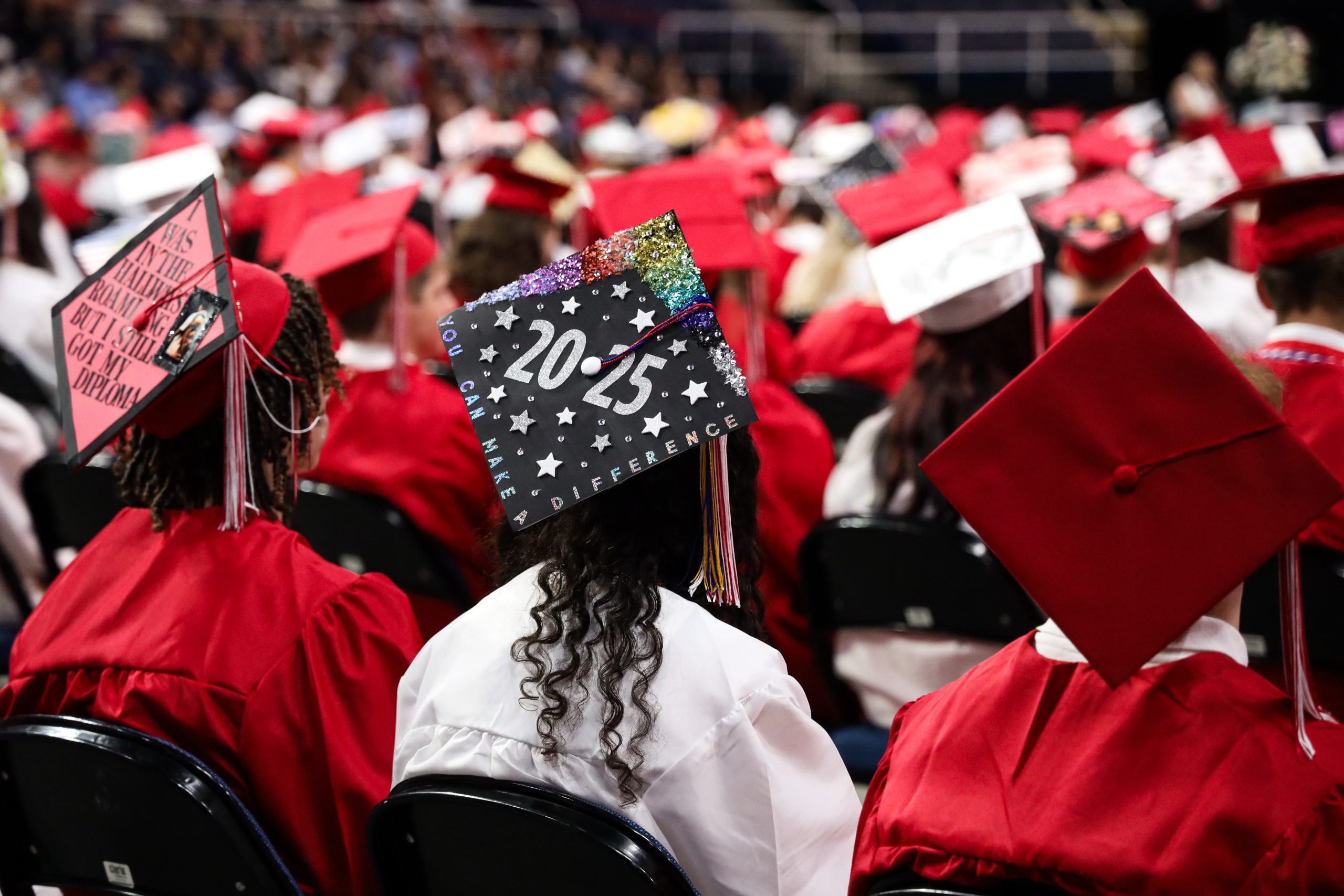 Graduates are seated in rows. Photo is a close up on the cap of a grad that's decorated with stars and says 2025