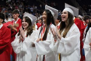 Graduates in white caps and gowns smile and clap