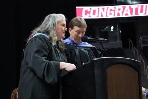 Two teachers wearing black robes speak at graduation