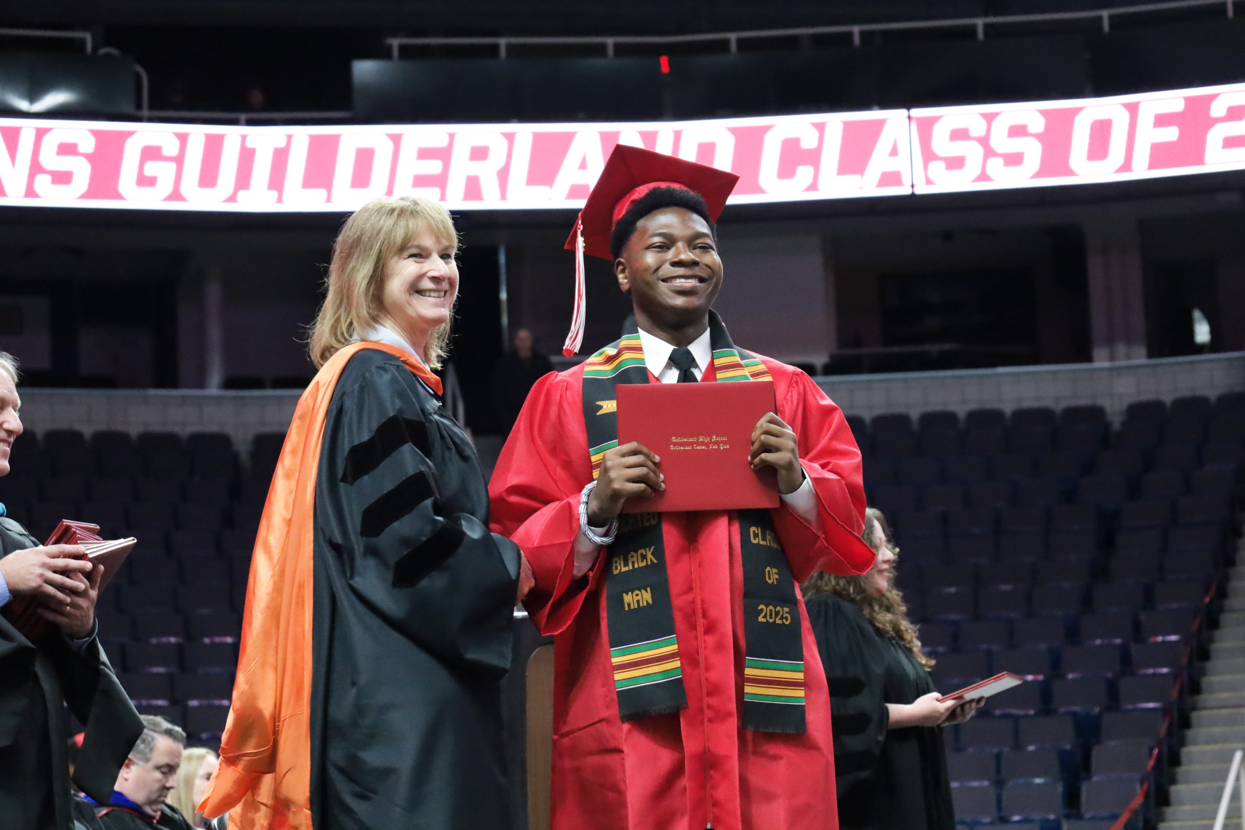 Standing next to the superintendent, a graduate proudly displays diploma, smiling
