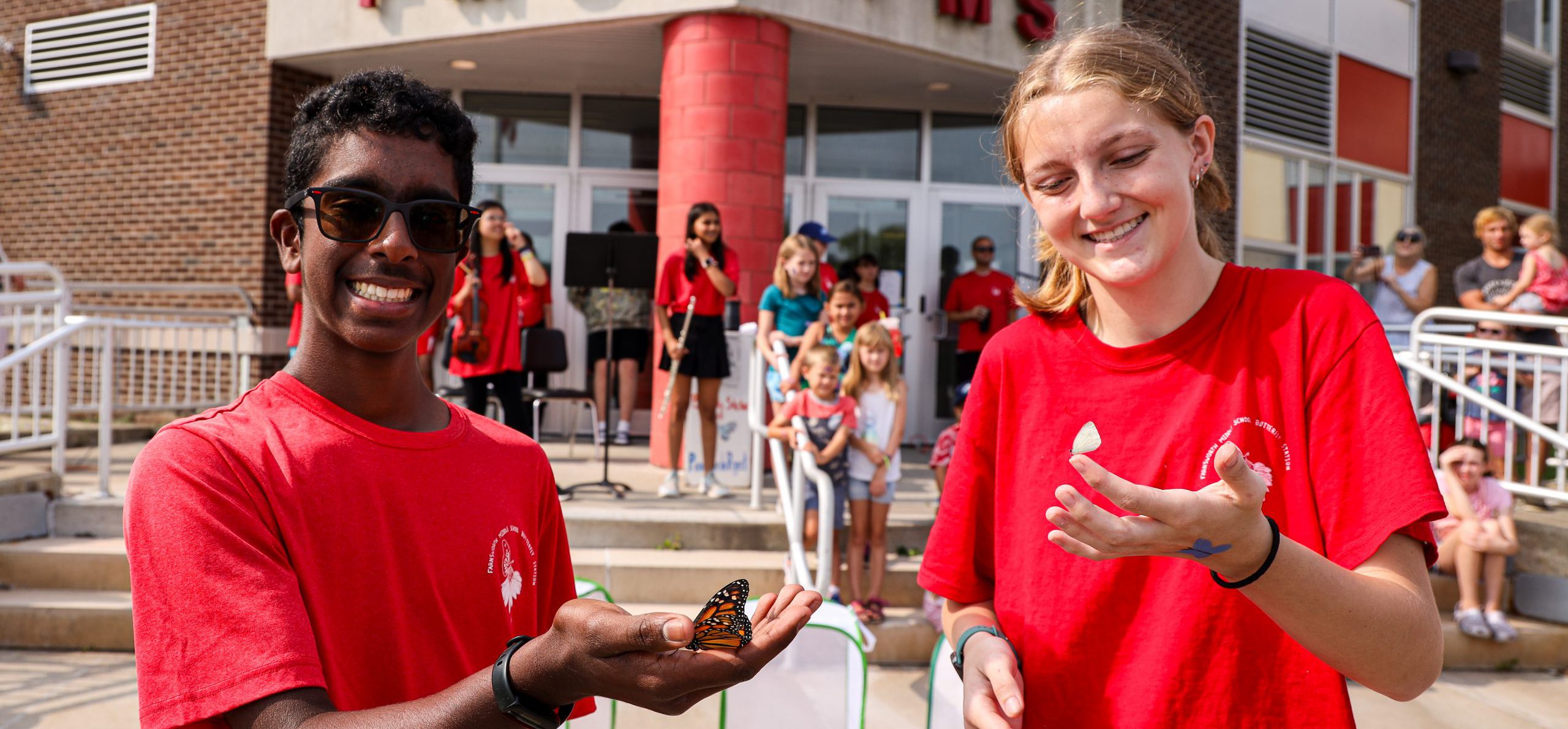 Two students smiling at camera while holding butterflies.